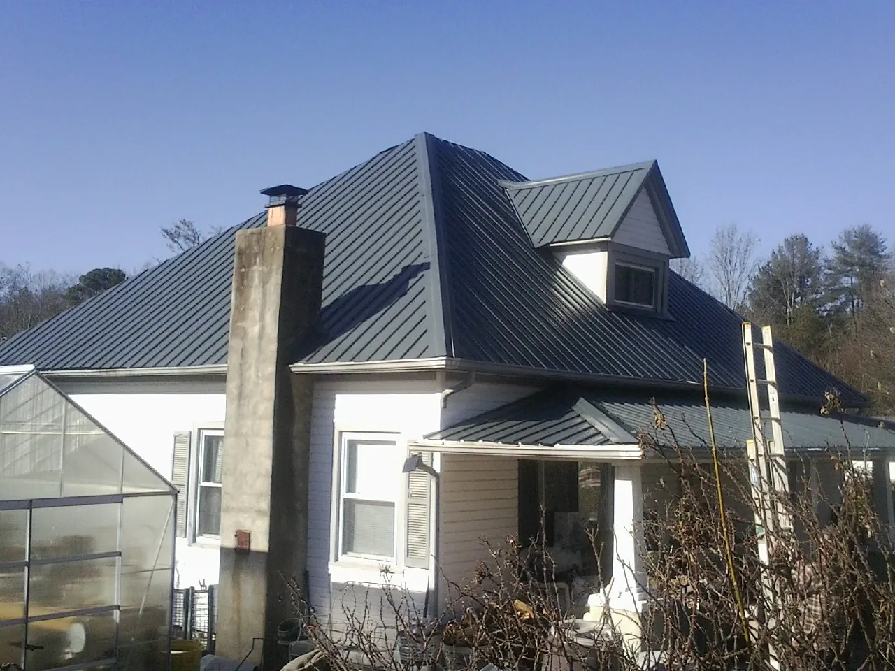 Dark blue standing seam metal roof on a white farmhouse with dormer — Slate & Tile Roof Repair by Roofing Brothers in Stover