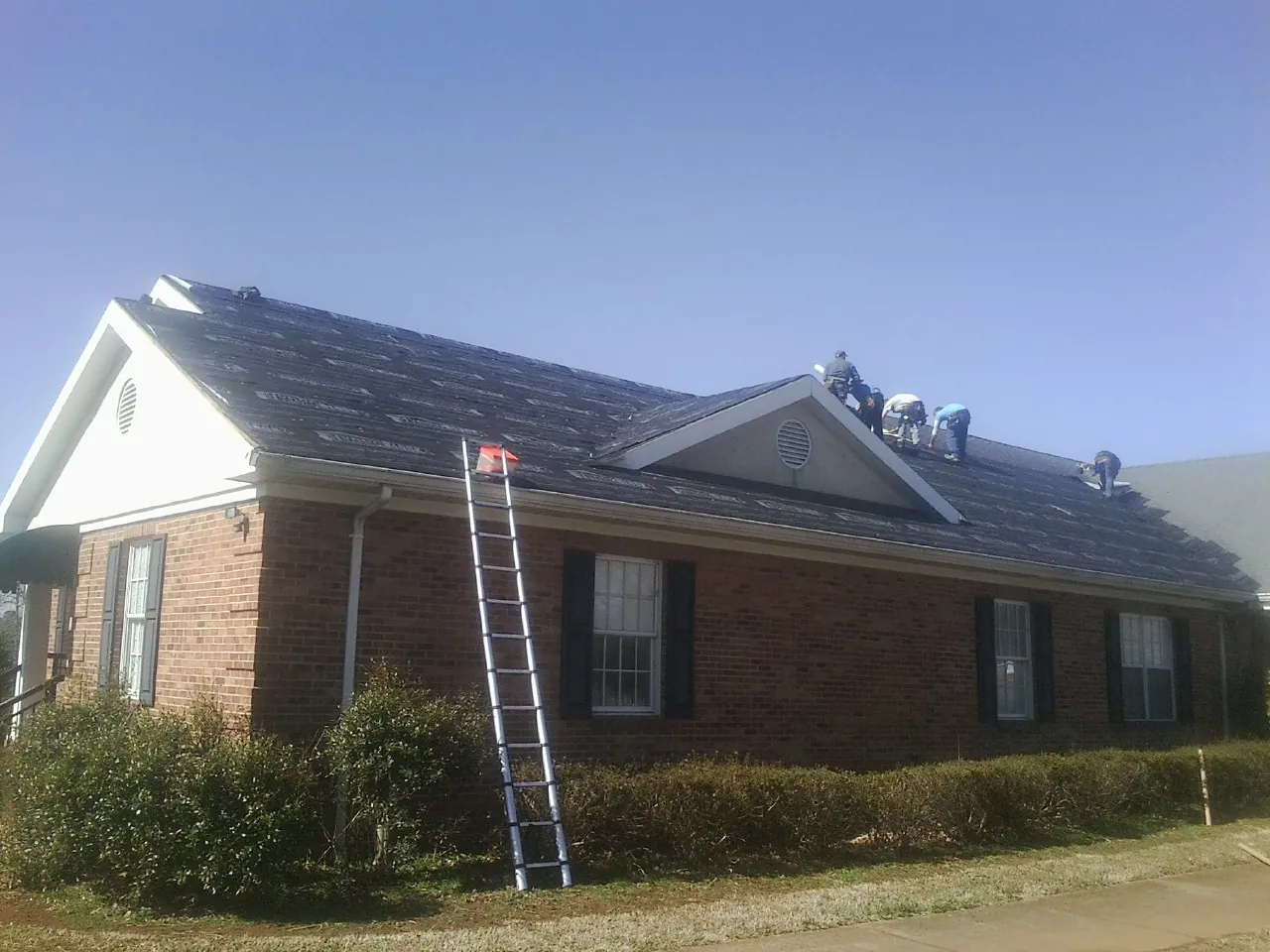 Crew tearing shingles off a brick ranch roof with a ladder set — Metal Roof Repair work by our crew in Stover