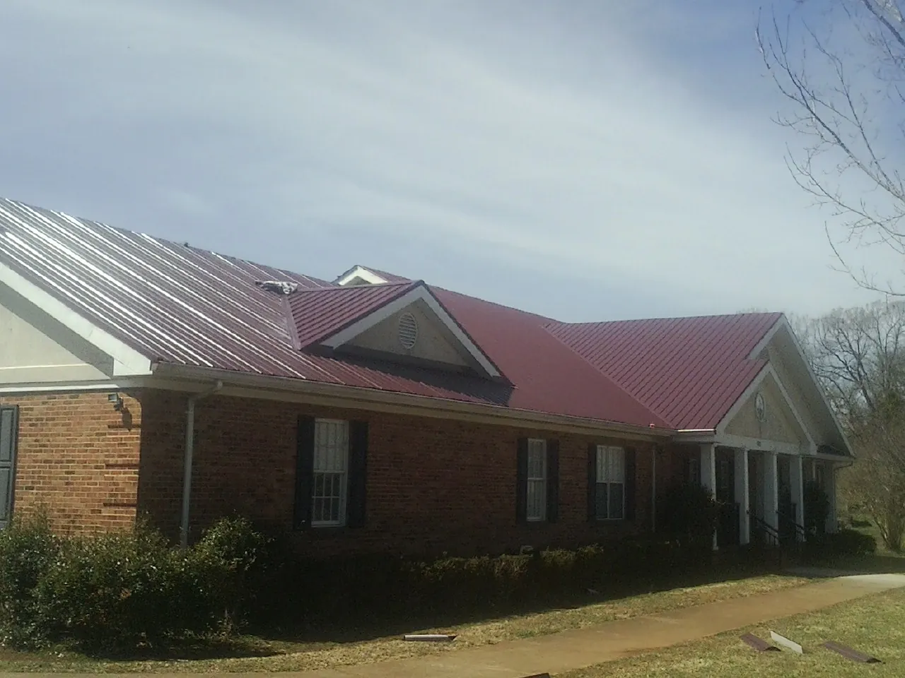 Red metal roof with gabled entries on a long brick building, from a Hail Damage Roof Repair job in Stover