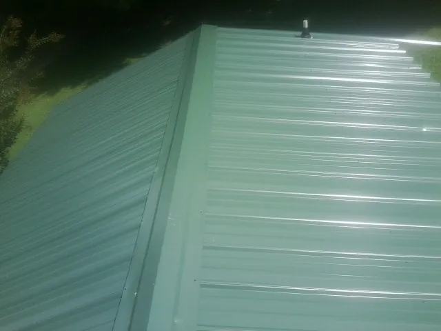 New green metal panels meeting at the ridge of a roof — Flat Roof Repair work by our crew in Stover