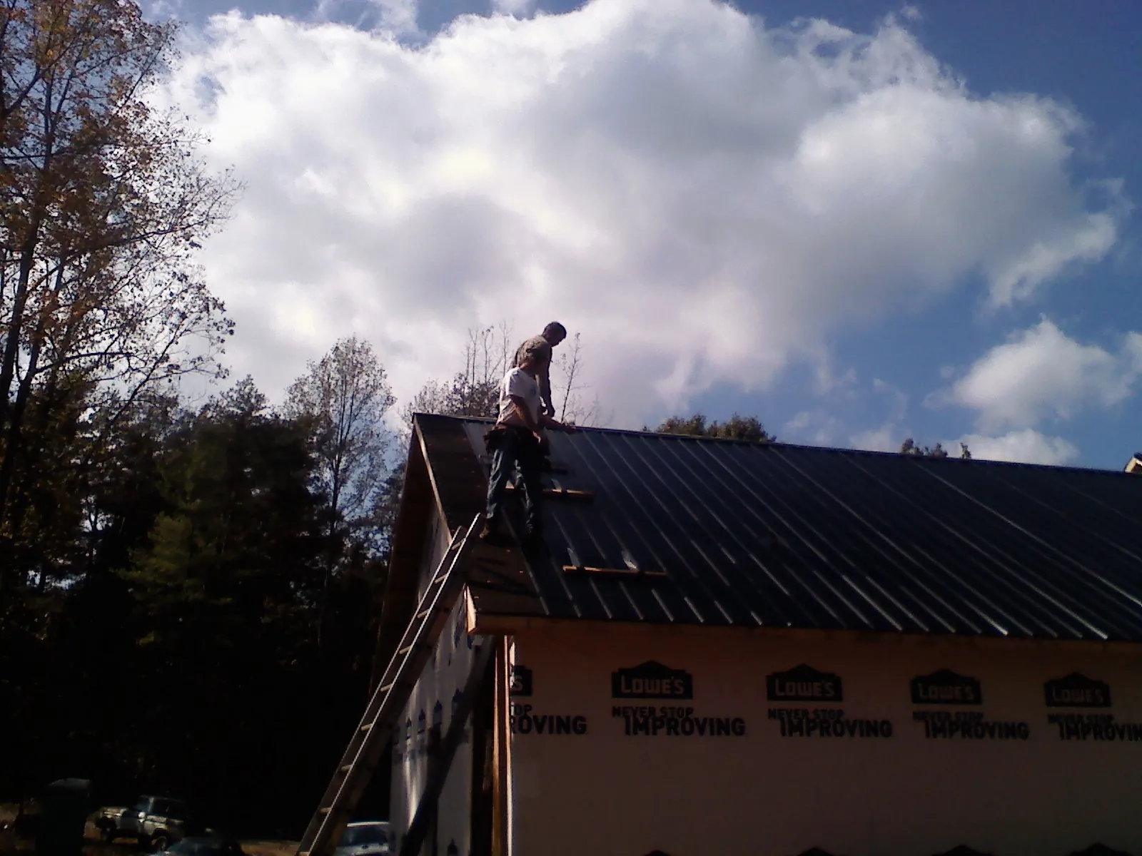 Roofer fastening dark metal panels high against a cloudy sky, from a Roof Inspection job in Stover