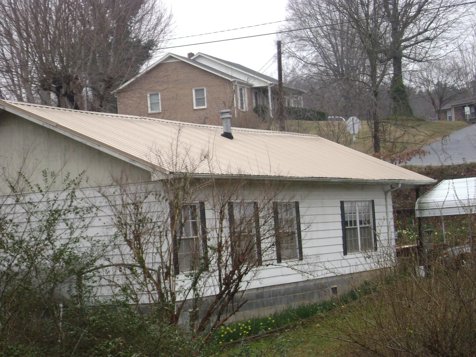 Tan metal roof on a white sided house set into a hillside — Commercial Roofing by Roofing Brothers in Stover
