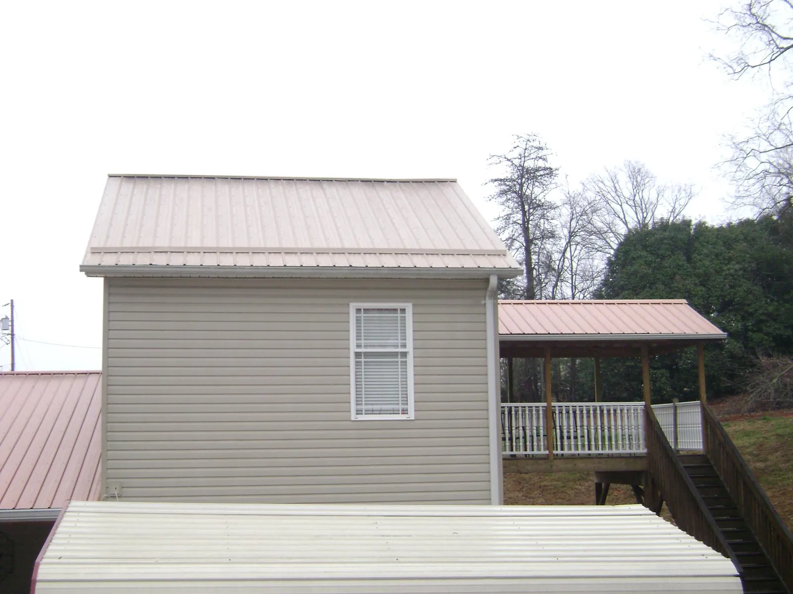 Tan metal roofs on a two story addition and attached porch, from a Roof Replacement job in Stover